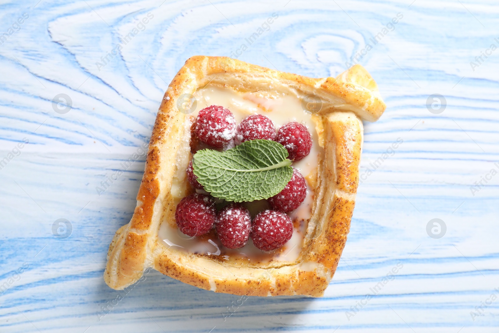 Photo of Tasty puff pastry with raspberries and mint on light blue wooden table, top view