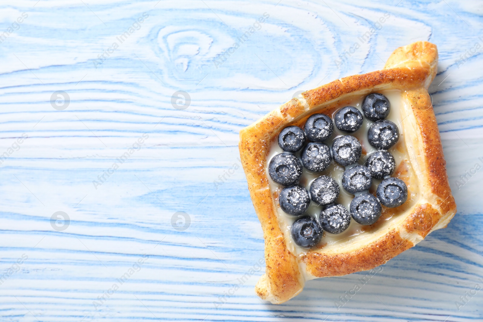 Photo of Tasty puff pastry with blueberries on light blue wooden table, top view. Space for text