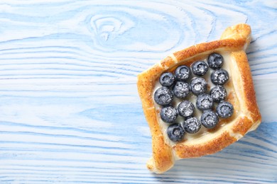 Tasty puff pastry with blueberries on light blue wooden table, top view. Space for text