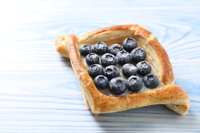 Tasty puff pastry with blueberries on light blue wooden table, closeup. Space for text