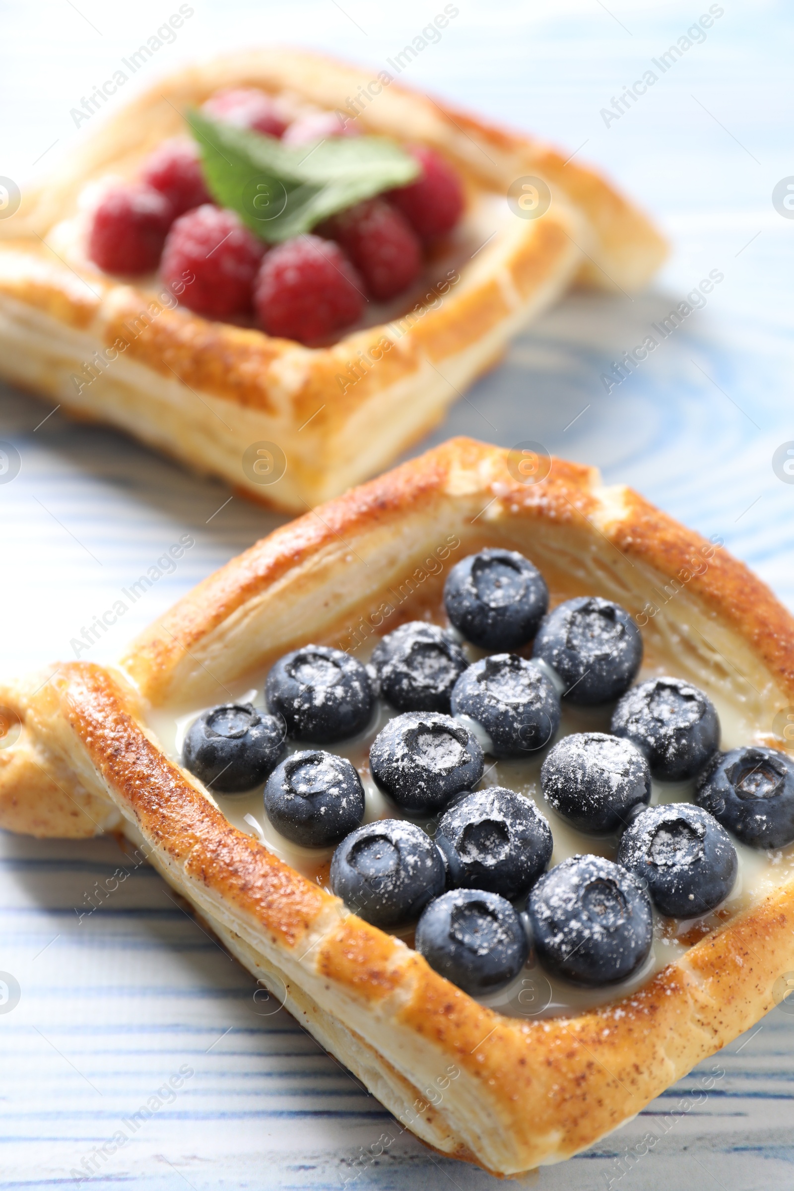 Photo of Tasty puff pastries with berries on light blue wooden table, closeup