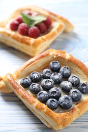 Photo of Tasty puff pastries with berries on light blue wooden table, closeup