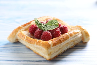 Photo of Tasty puff pastry with raspberries and mint on light blue wooden table