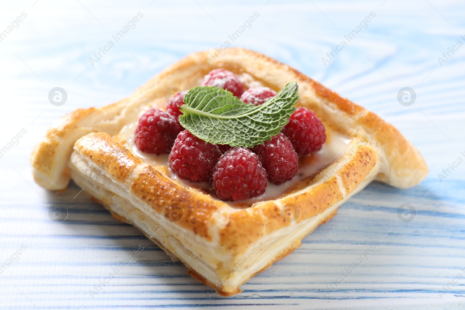 Photo of Tasty puff pastry with raspberries and mint on light blue wooden table