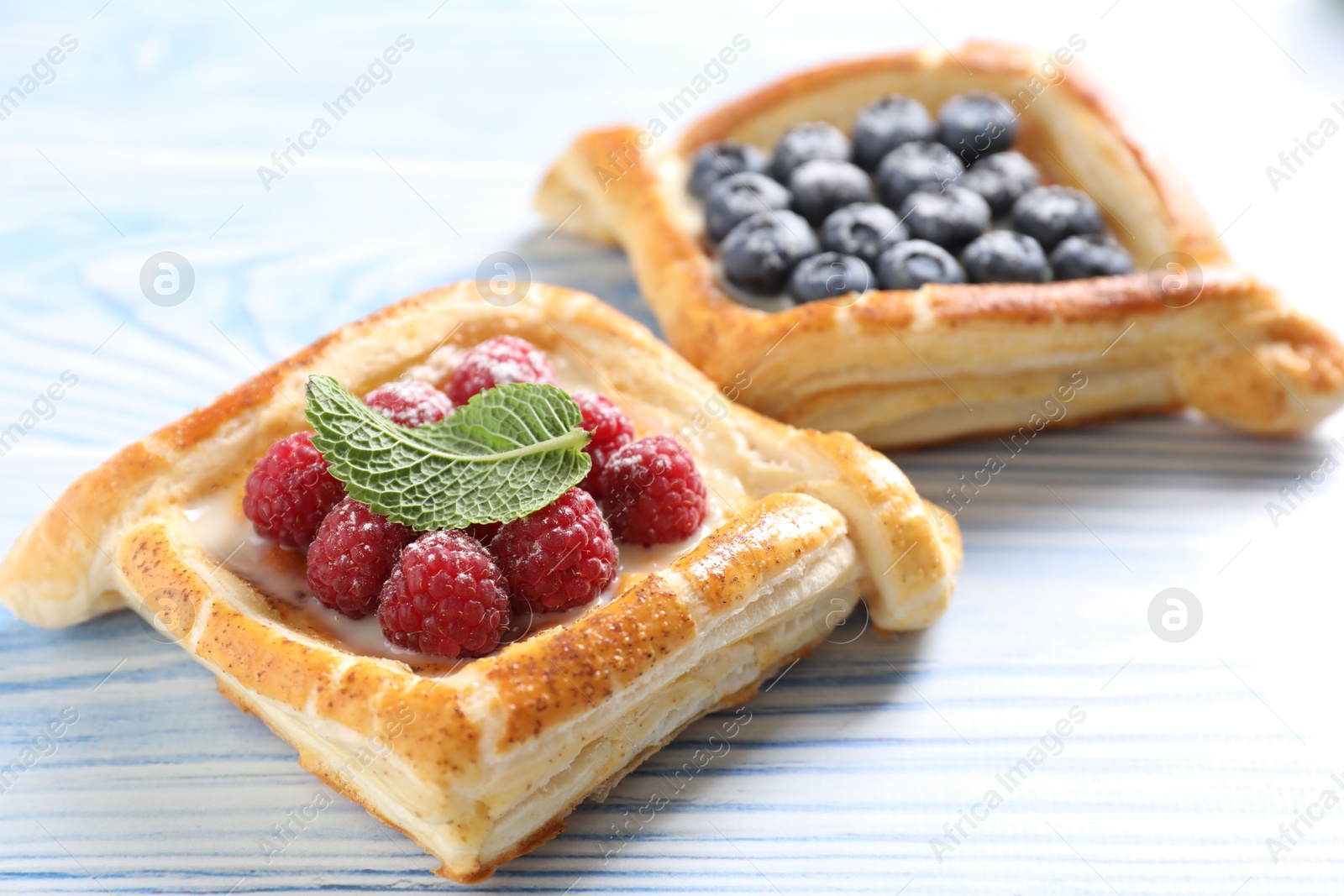 Photo of Tasty puff pastries with berries on light blue wooden table, closeup