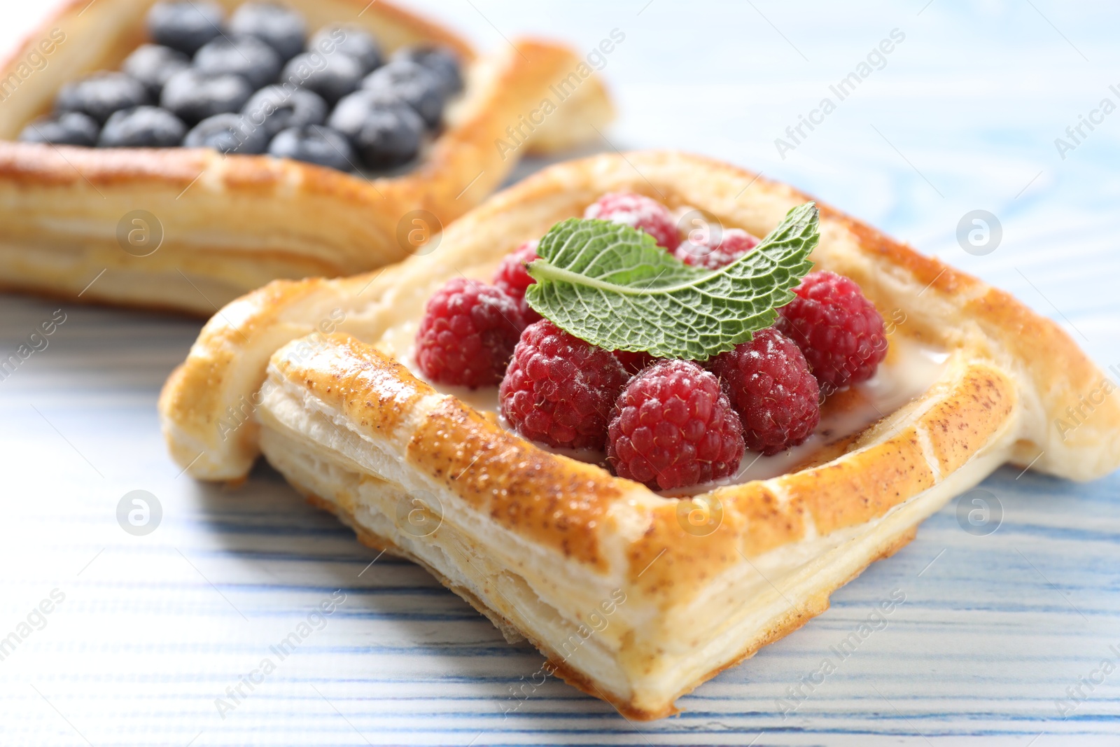 Photo of Tasty puff pastries with berries on light blue wooden table, closeup