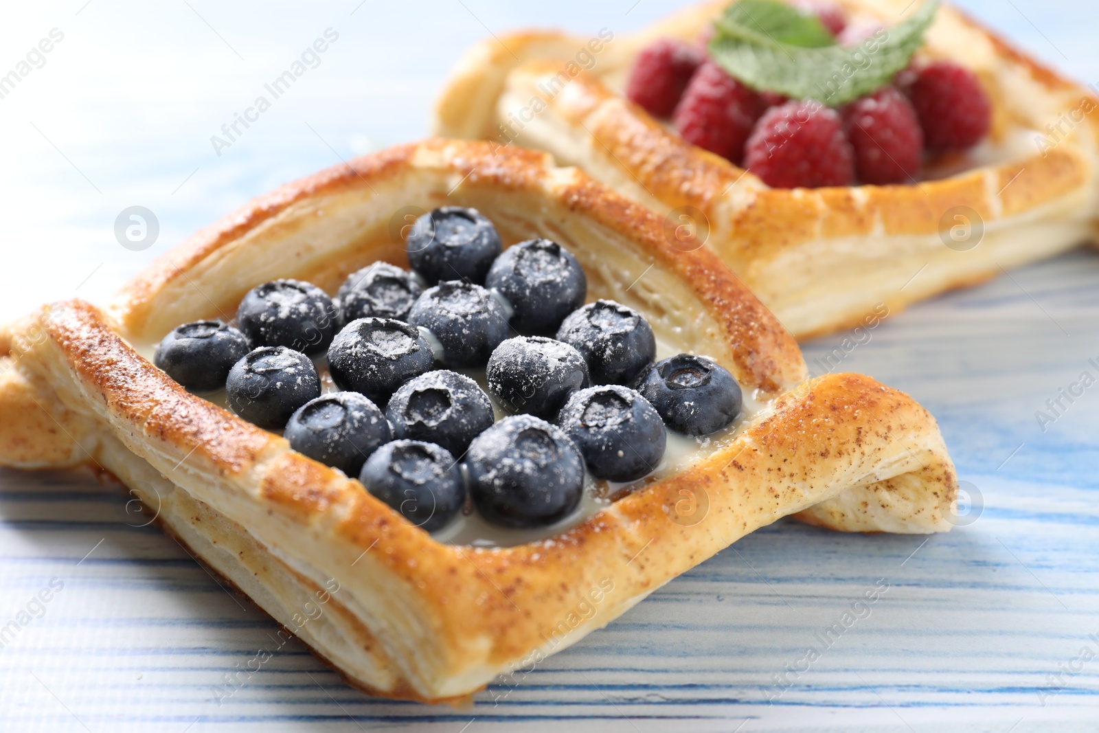 Photo of Tasty puff pastries with berries on light blue wooden table, closeup