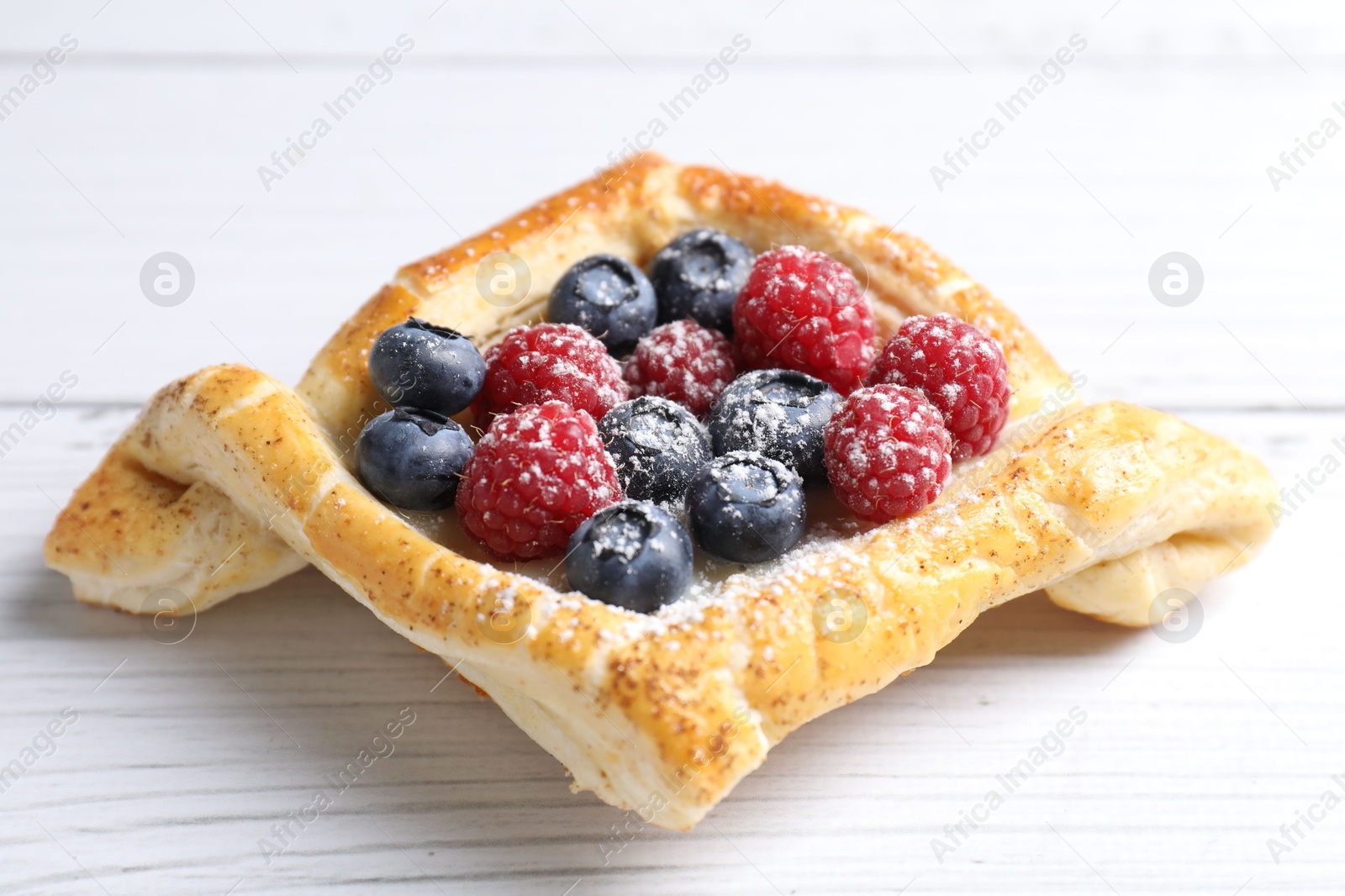 Photo of Tasty puff pastry with berries on white wooden table, closeup