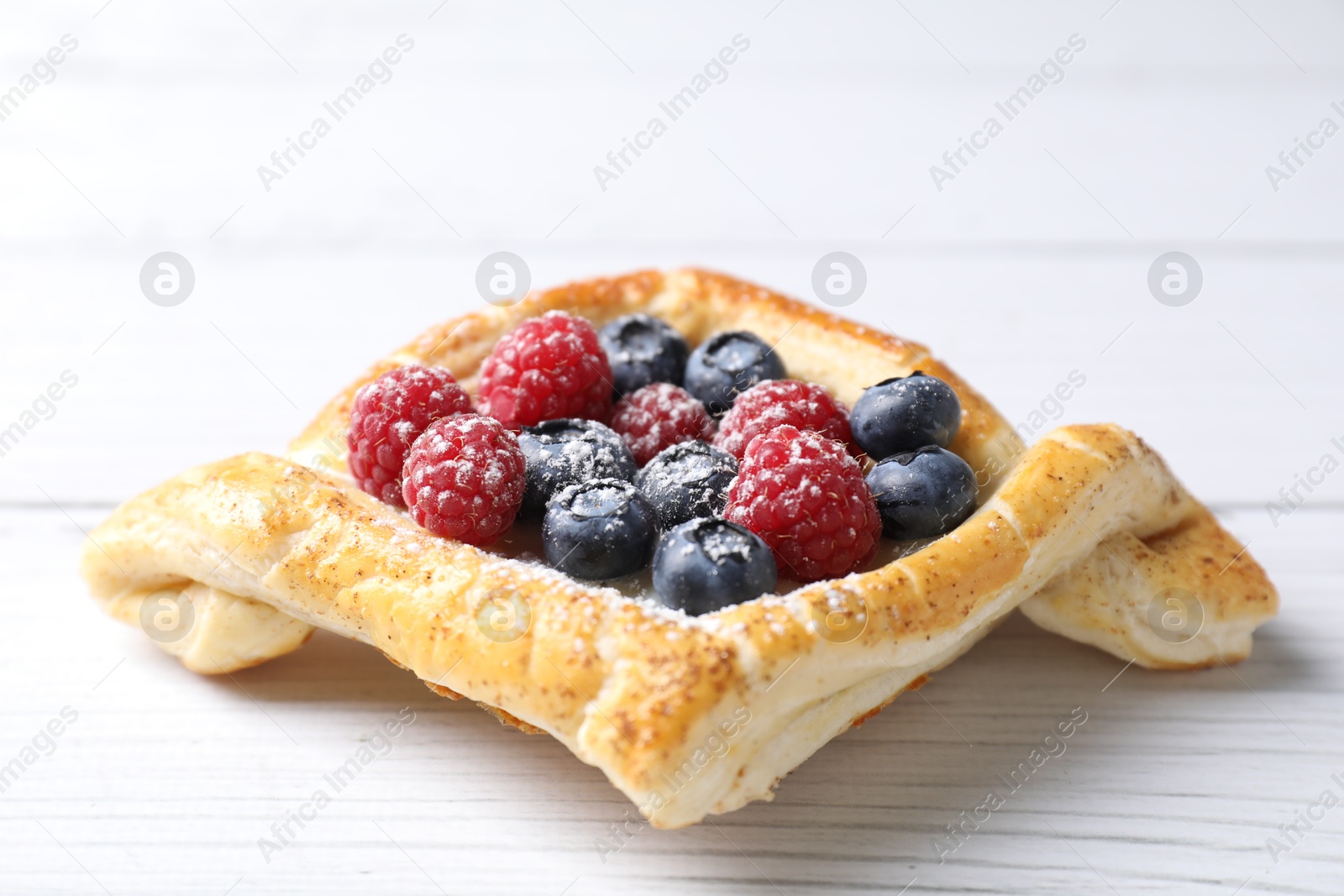 Photo of Tasty puff pastry with berries on white wooden table, closeup