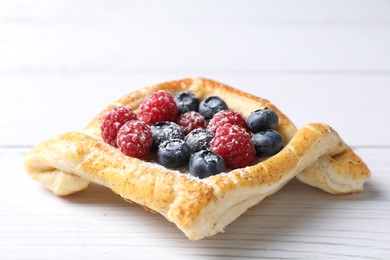 Tasty puff pastry with berries on white wooden table, closeup