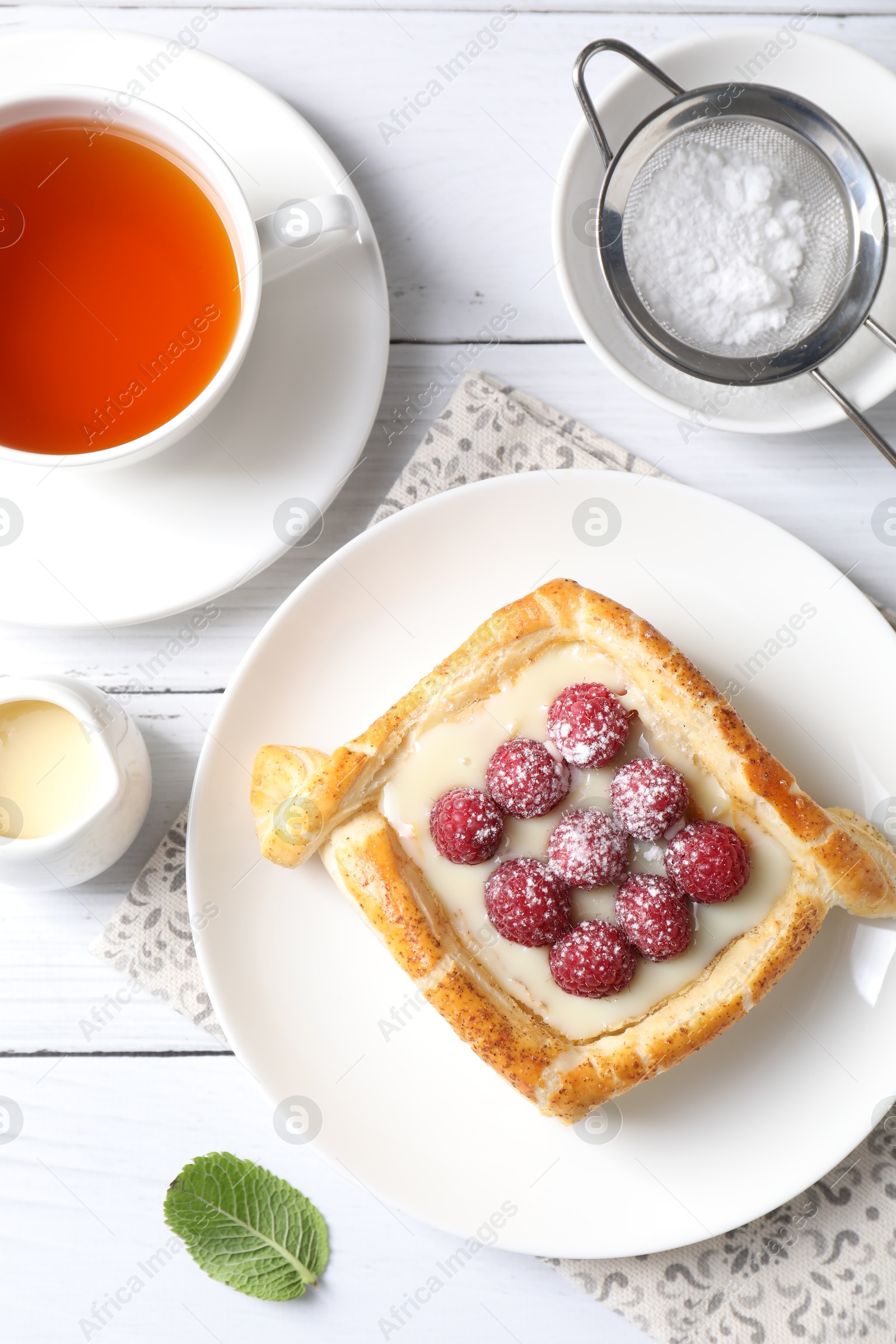 Photo of Tasty puff pastry with raspberries and tea on white wooden table, flat lay