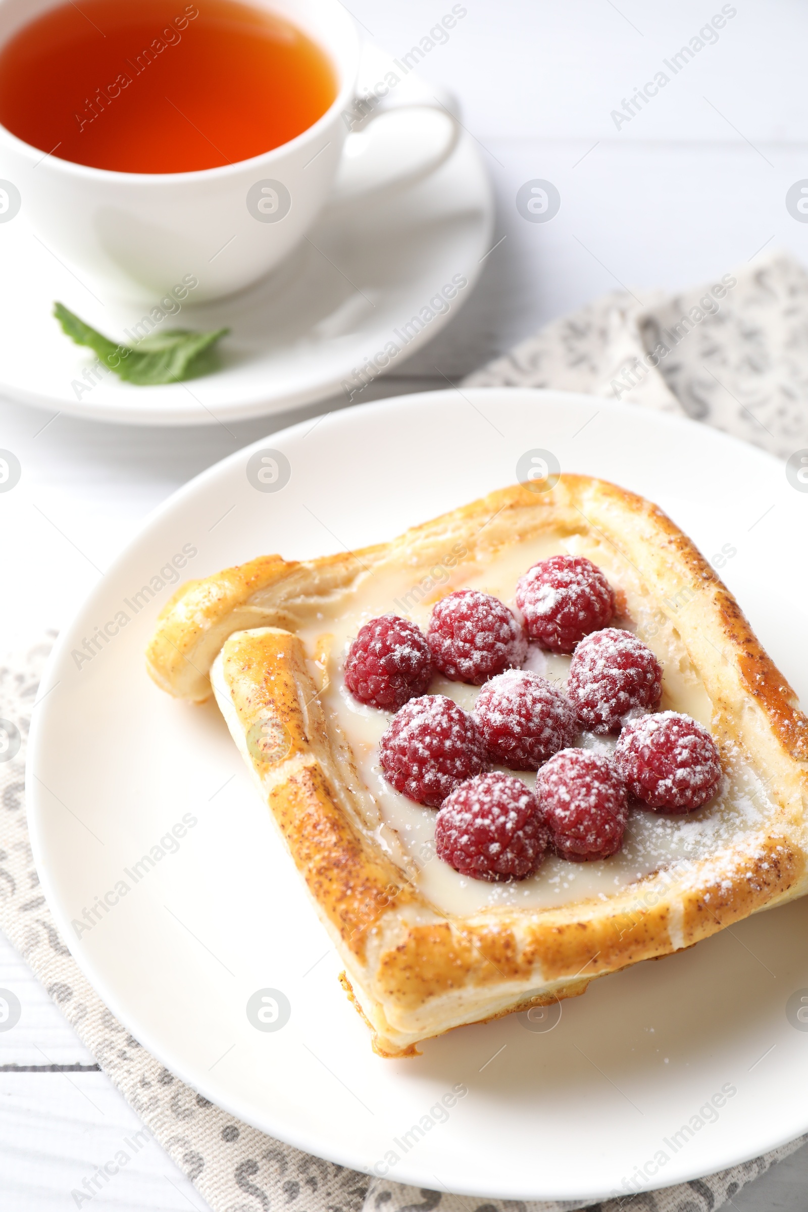 Photo of Tasty puff pastry with raspberries and tea on white wooden table, closeup