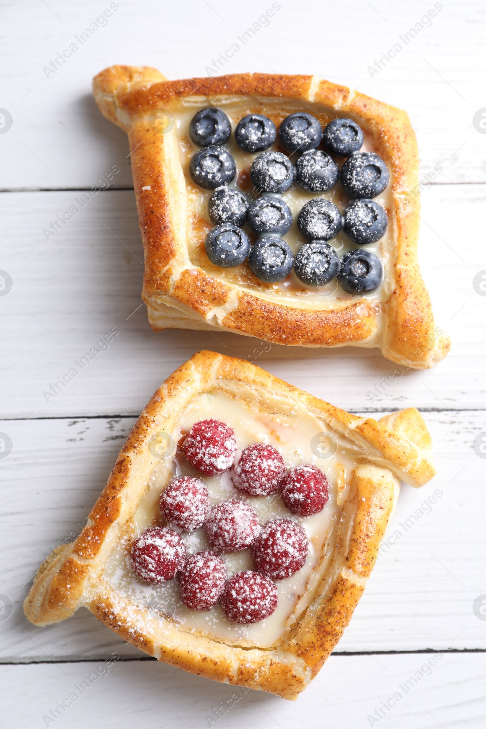 Photo of Tasty puff pastries with berries on white wooden table, top view