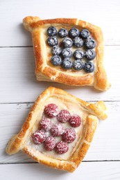 Photo of Tasty puff pastries with berries on white wooden table, top view