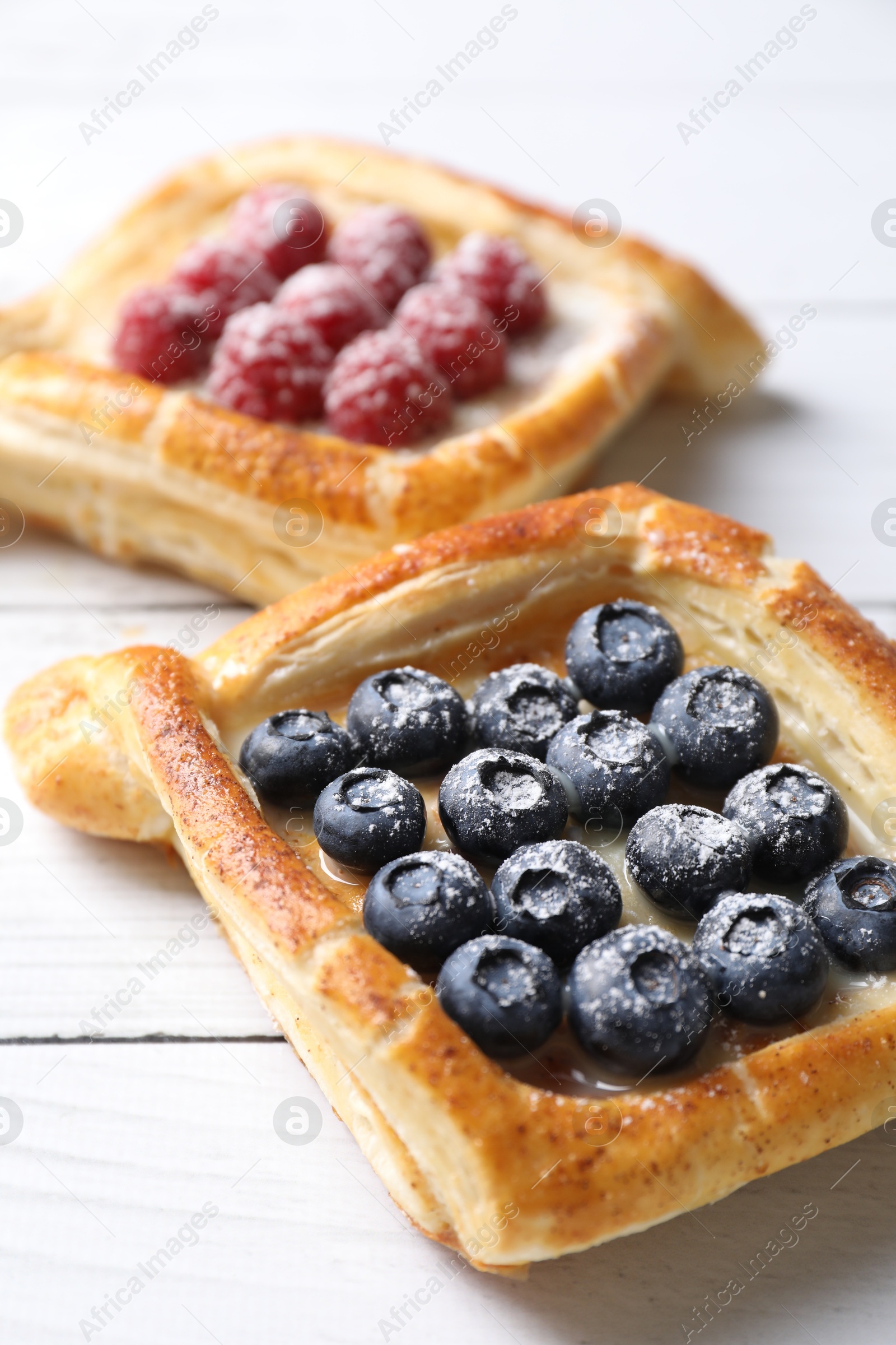 Photo of Tasty puff pastries with berries on white wooden table, closeup