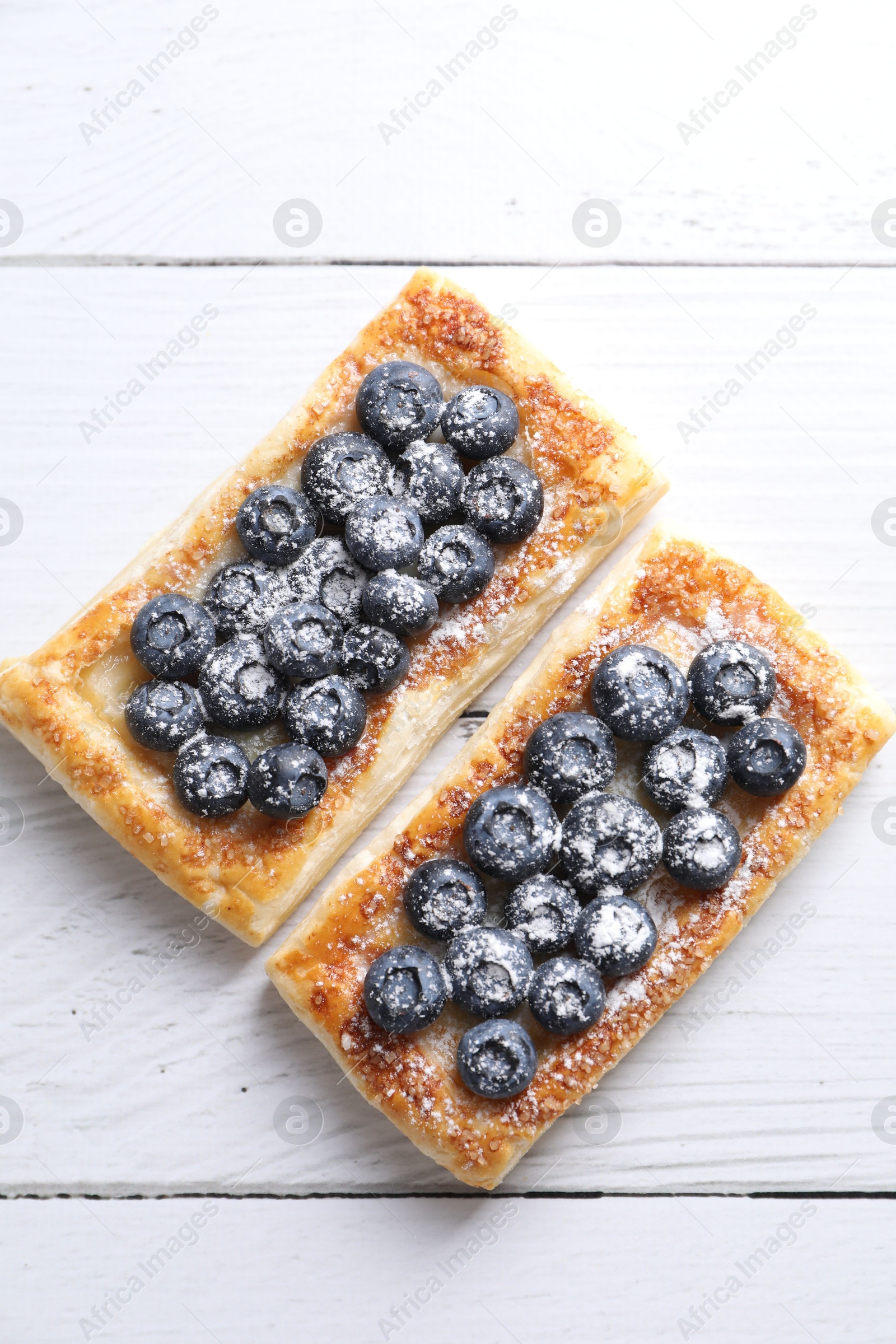 Photo of Tasty puff pastries with blueberries on white wooden table, flat lay