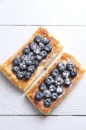 Photo of Tasty puff pastries with blueberries on white wooden table, flat lay