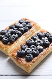 Photo of Tasty puff pastries with blueberries on white wooden table, closeup