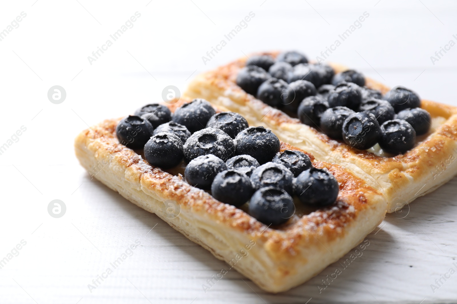 Photo of Tasty puff pastries with blueberries on white wooden table, closeup