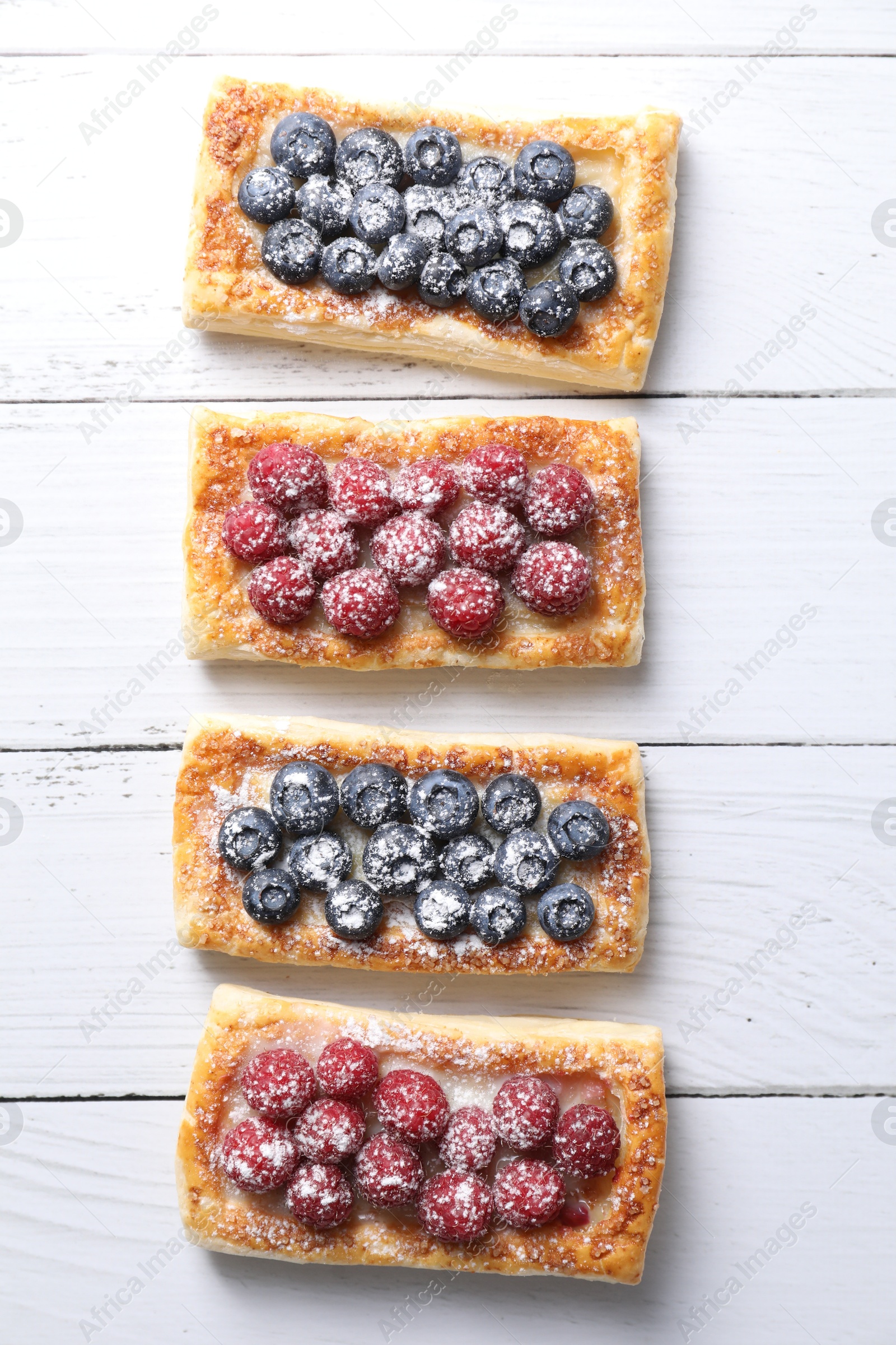 Photo of Tasty puff pastries with berries on white wooden table, flat lay