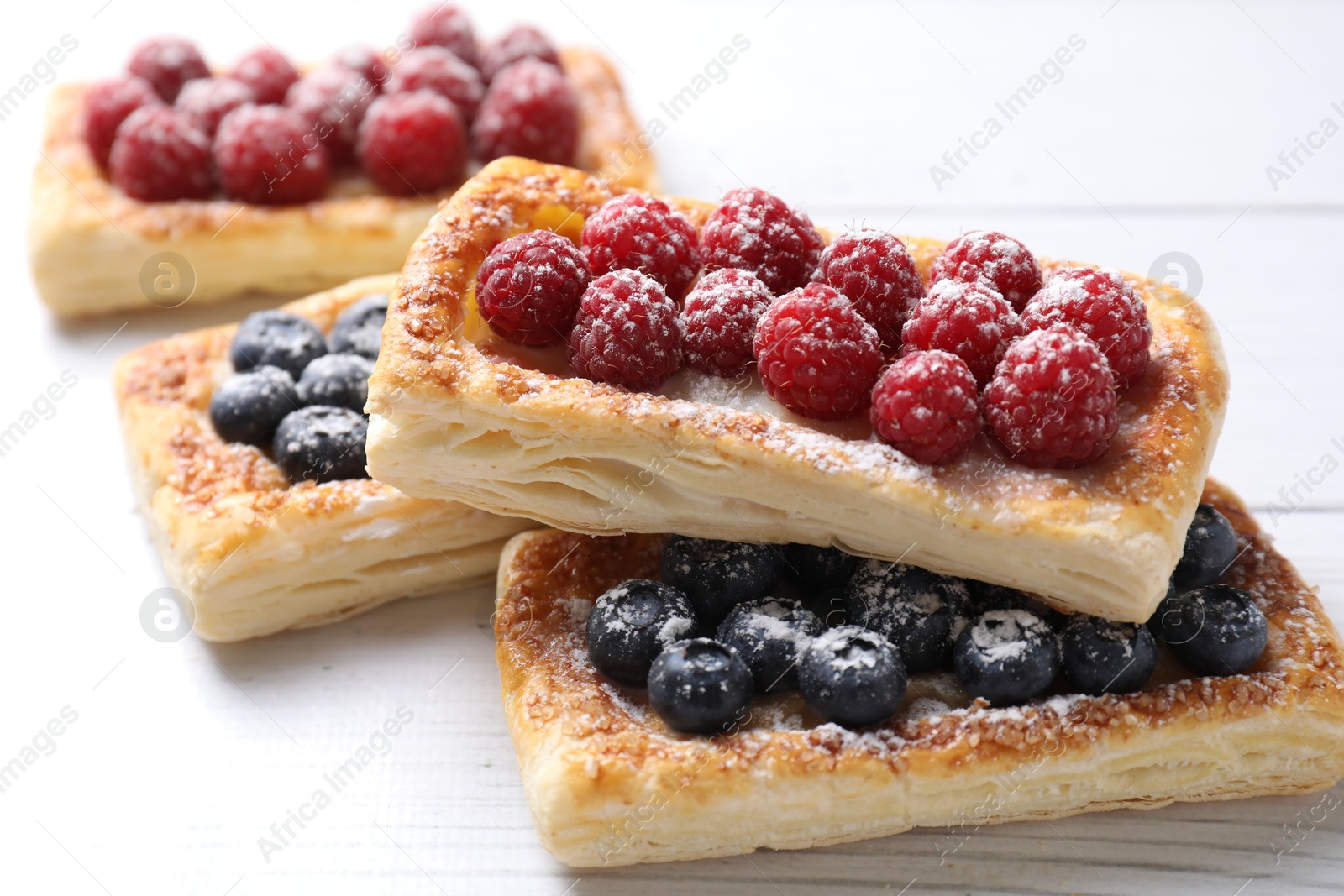 Photo of Tasty puff pastries with berries on white wooden table, closeup