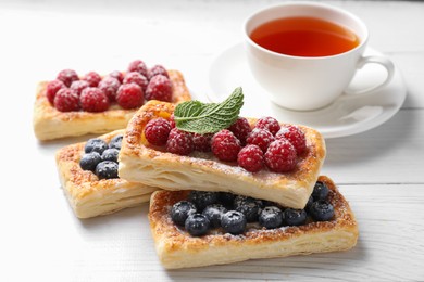 Photo of Tasty puff pastries with berries and tea on white wooden table, closeup