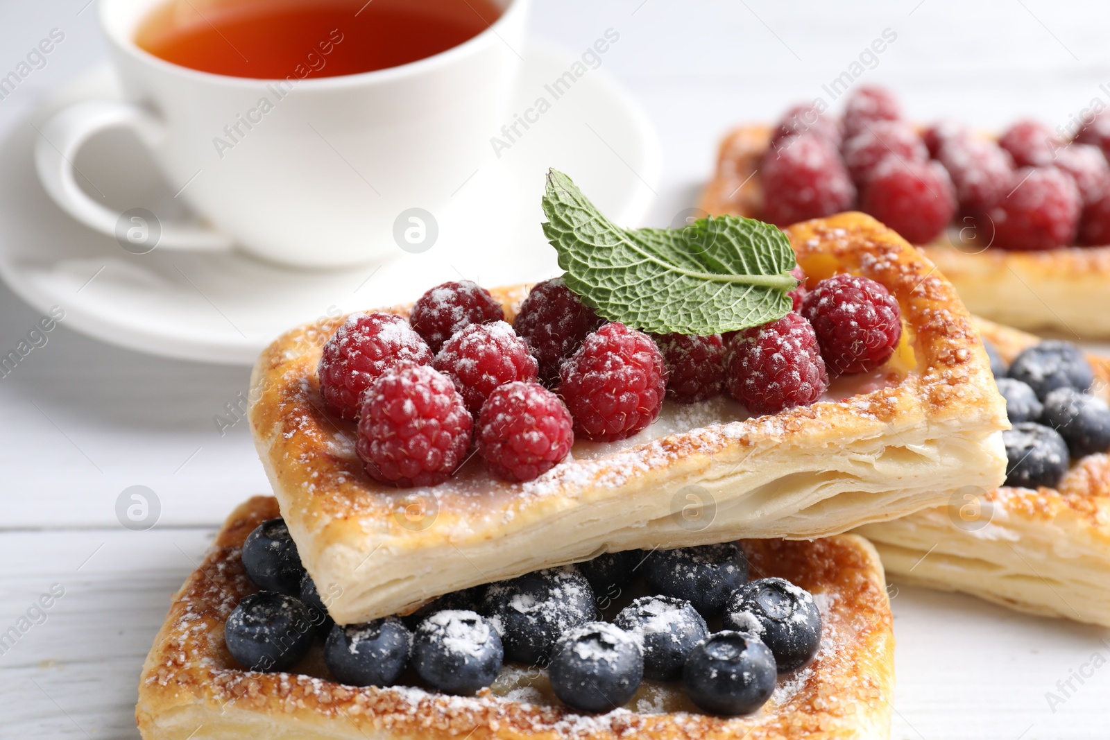 Photo of Tasty puff pastries with berries and tea on white wooden table, closeup