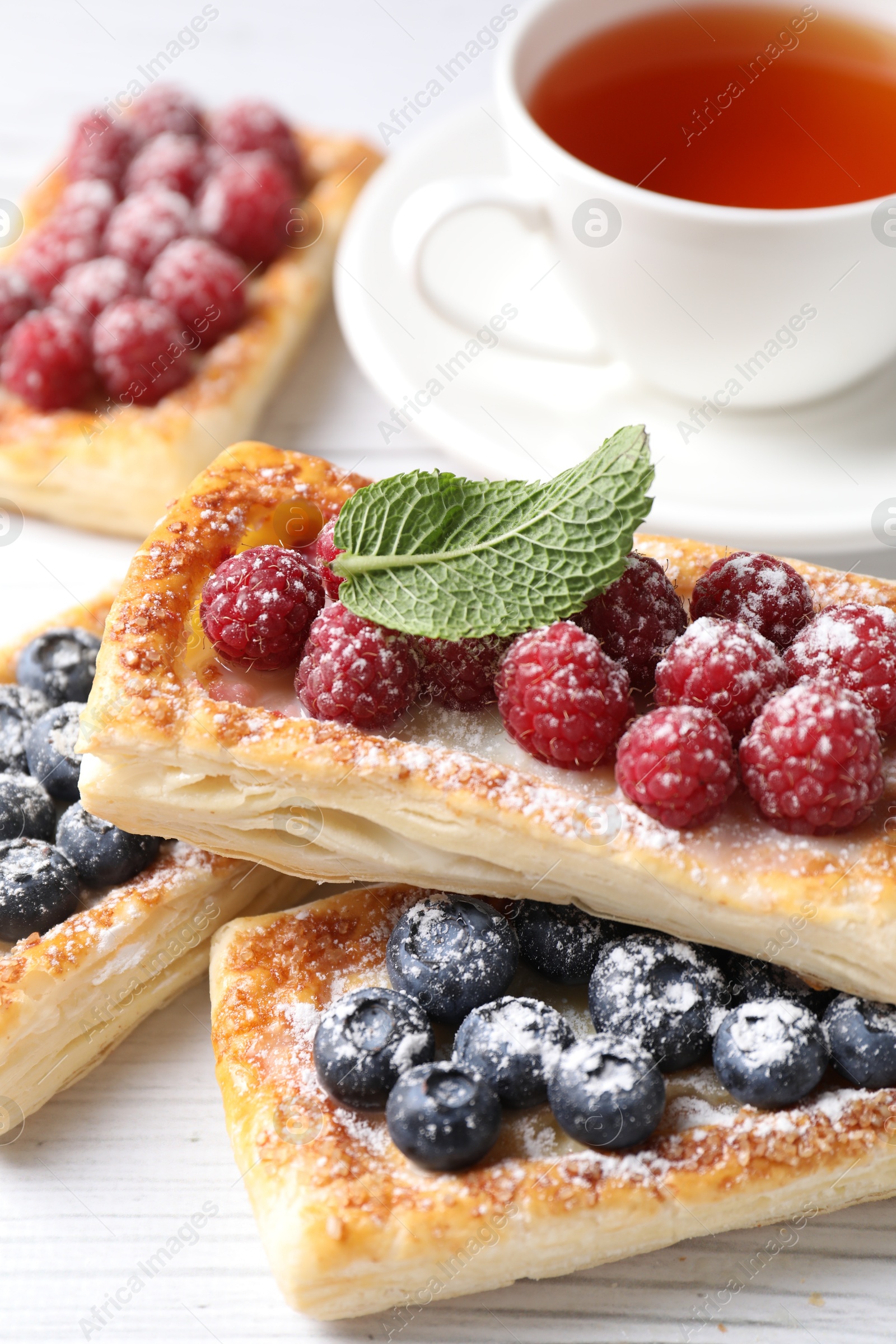 Photo of Tasty puff pastries with berries and tea on white wooden table, closeup