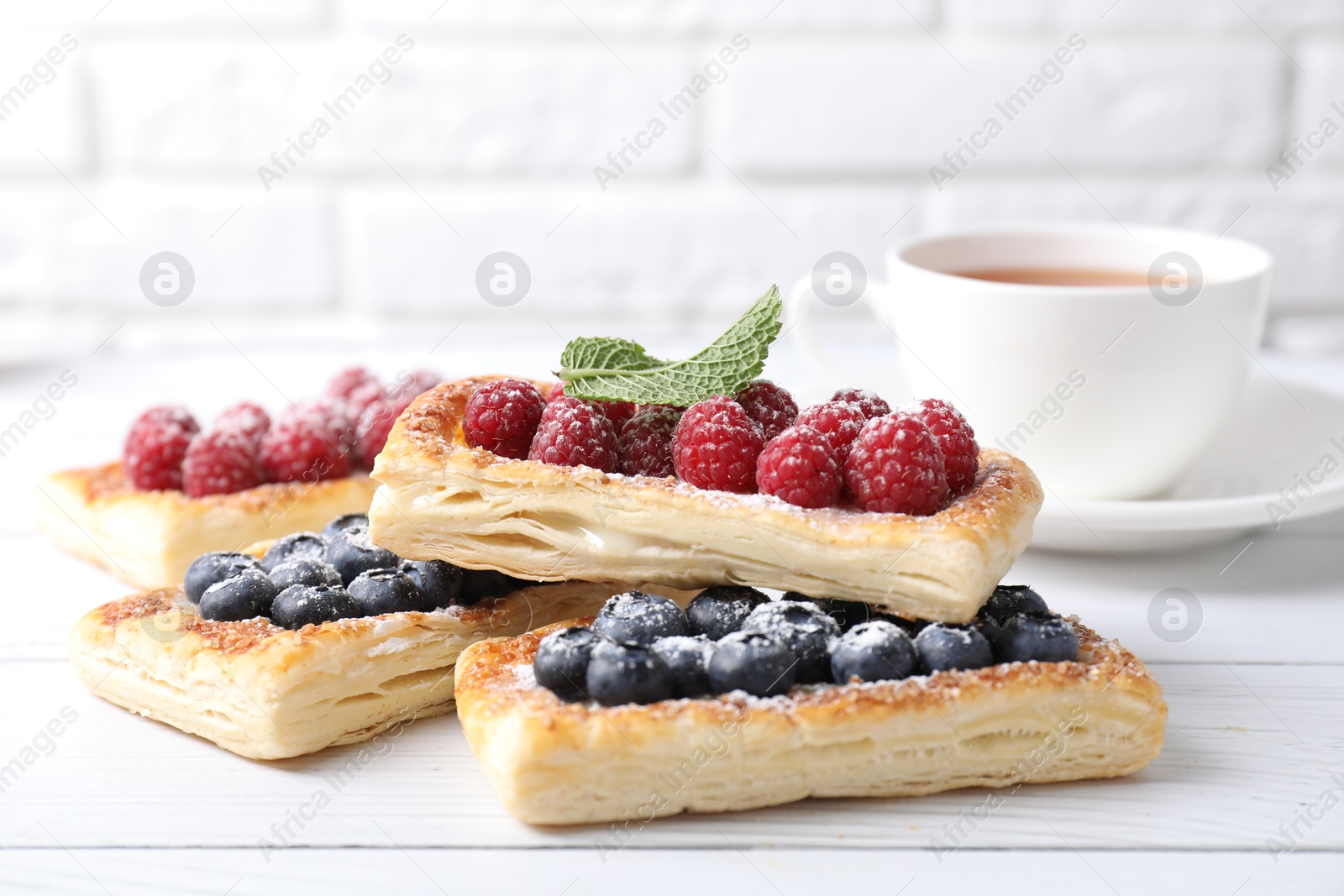 Photo of Tasty puff pastries with berries and tea on white wooden table, closeup