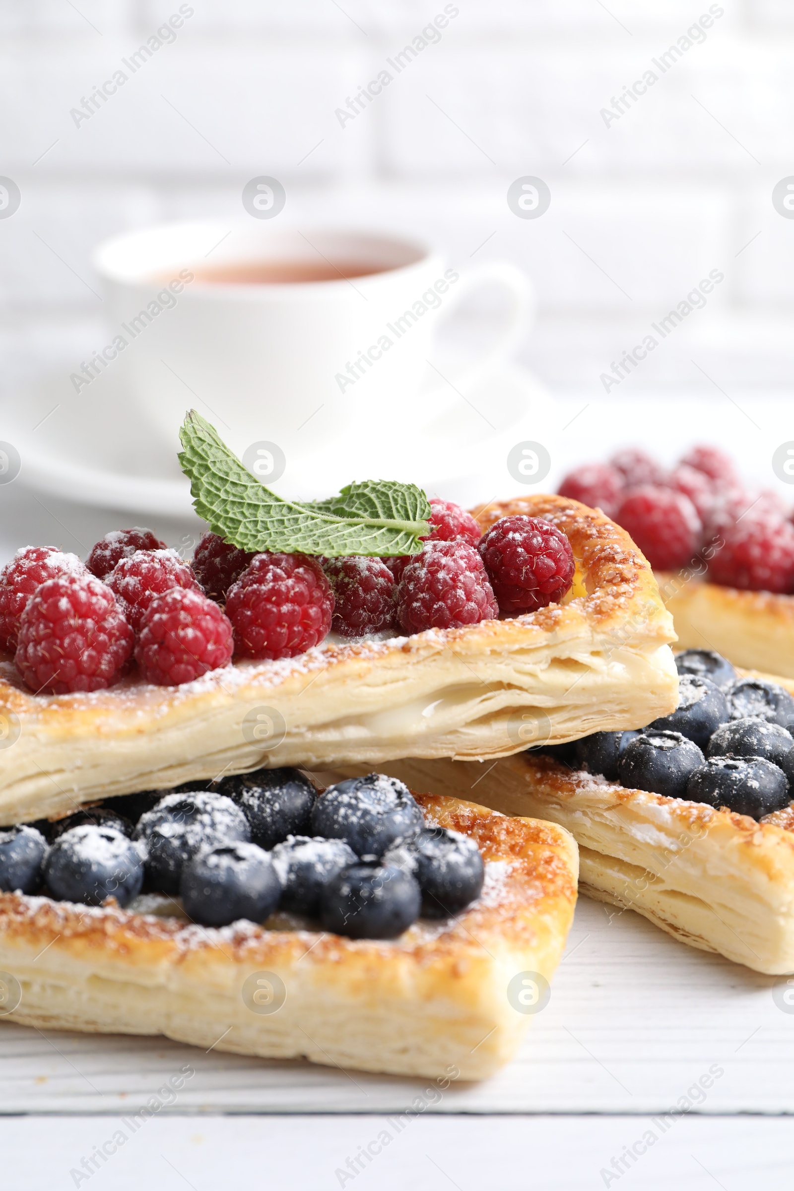 Photo of Tasty puff pastries with berries and tea on white wooden table, closeup