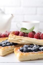 Tasty puff pastries with berries on white wooden table, closeup