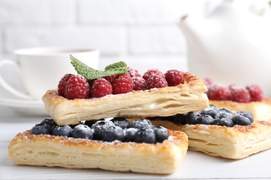 Tasty puff pastries with berries on white wooden table, closeup