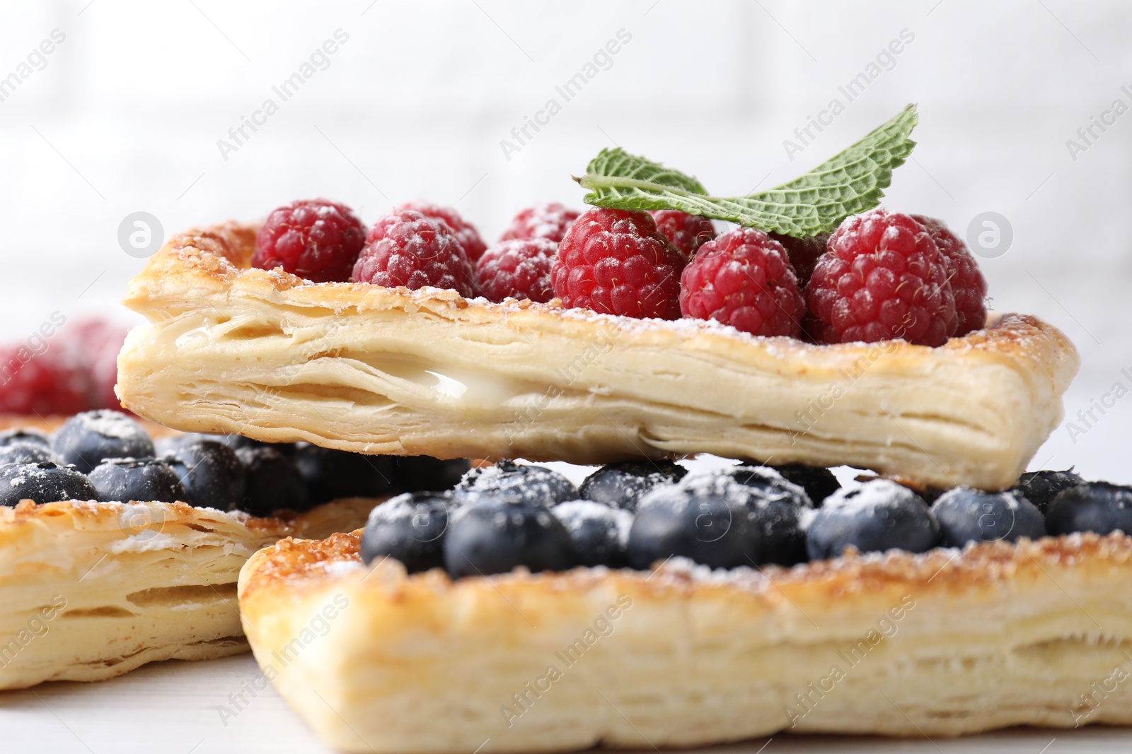 Photo of Tasty puff pastries with berries on white wooden table, closeup