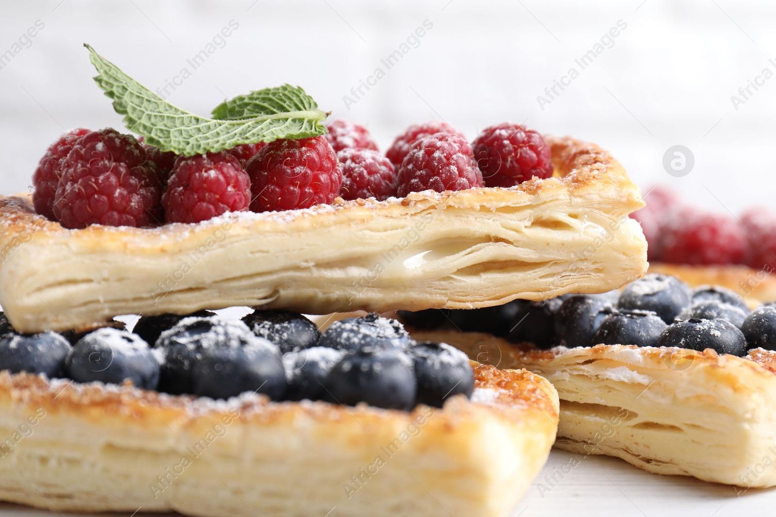 Photo of Tasty puff pastries with berries on white wooden table, closeup