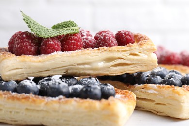 Tasty puff pastries with berries on white wooden table, closeup