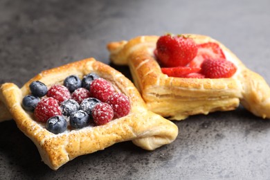 Tasty puff pastries with berries on grey table, closeup