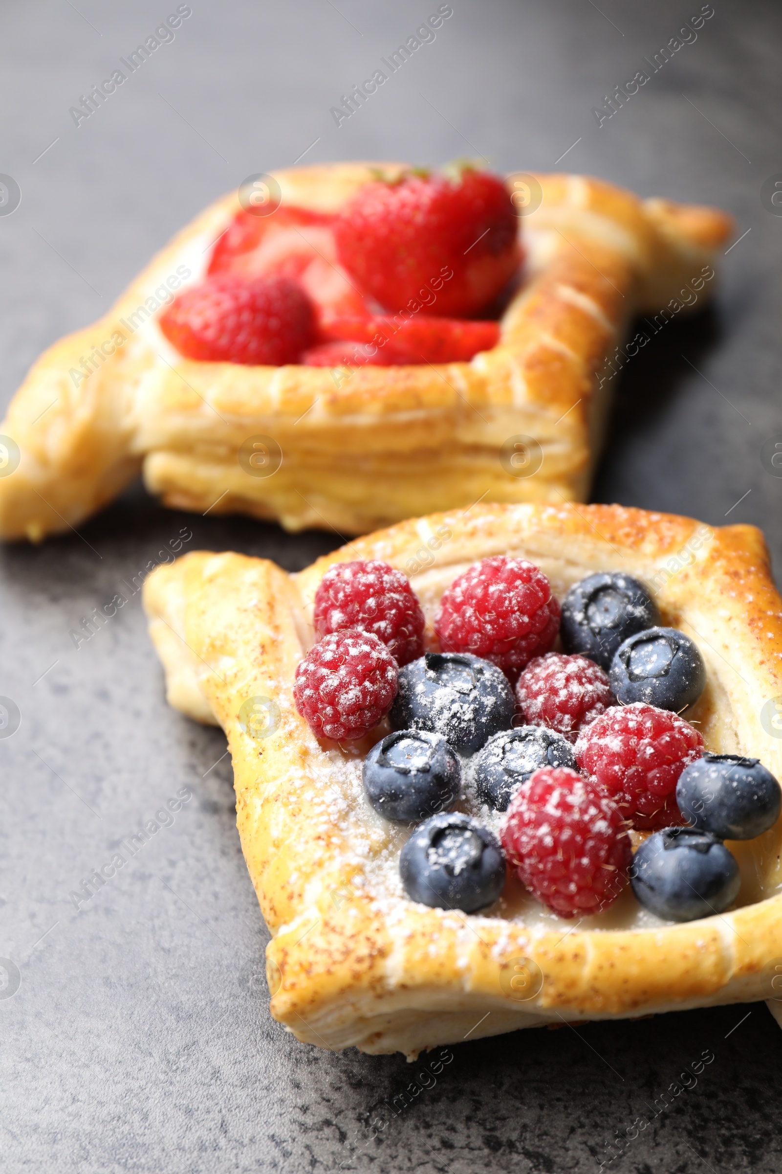 Photo of Tasty puff pastries with berries on grey table, closeup