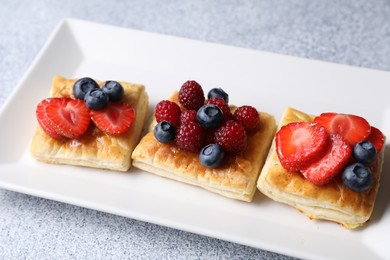 Photo of Tasty puff pastries with berries on light grey table, closeup