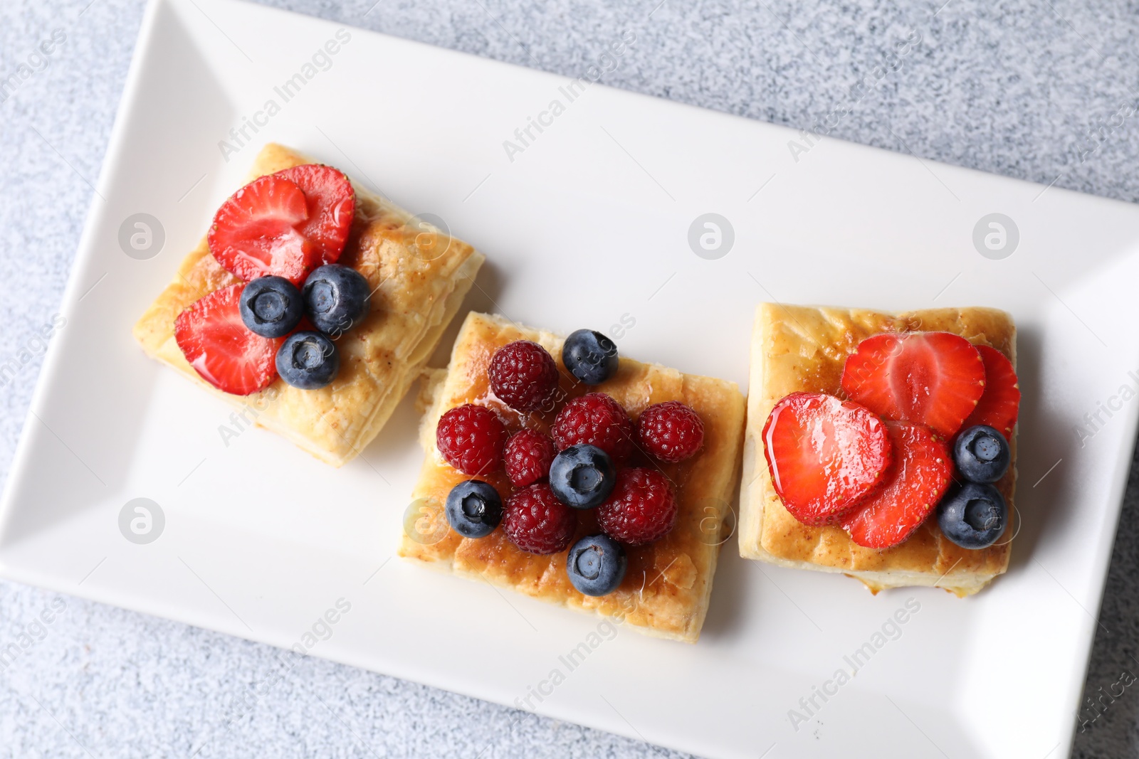 Photo of Tasty puff pastries with berries on light grey table, top view