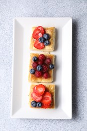 Photo of Tasty puff pastries with berries on light grey table, top view