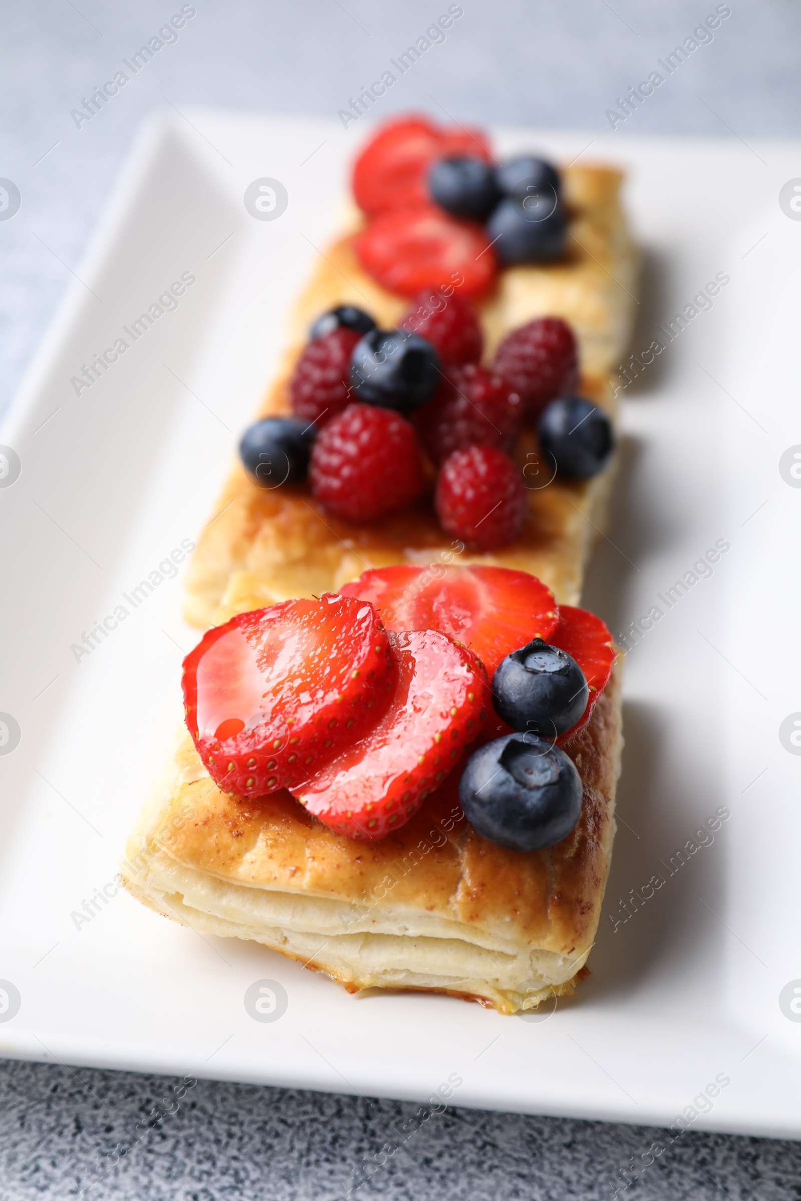 Photo of Tasty puff pastries with berries on light grey table, closeup