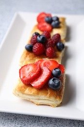 Photo of Tasty puff pastries with berries on light grey table, closeup