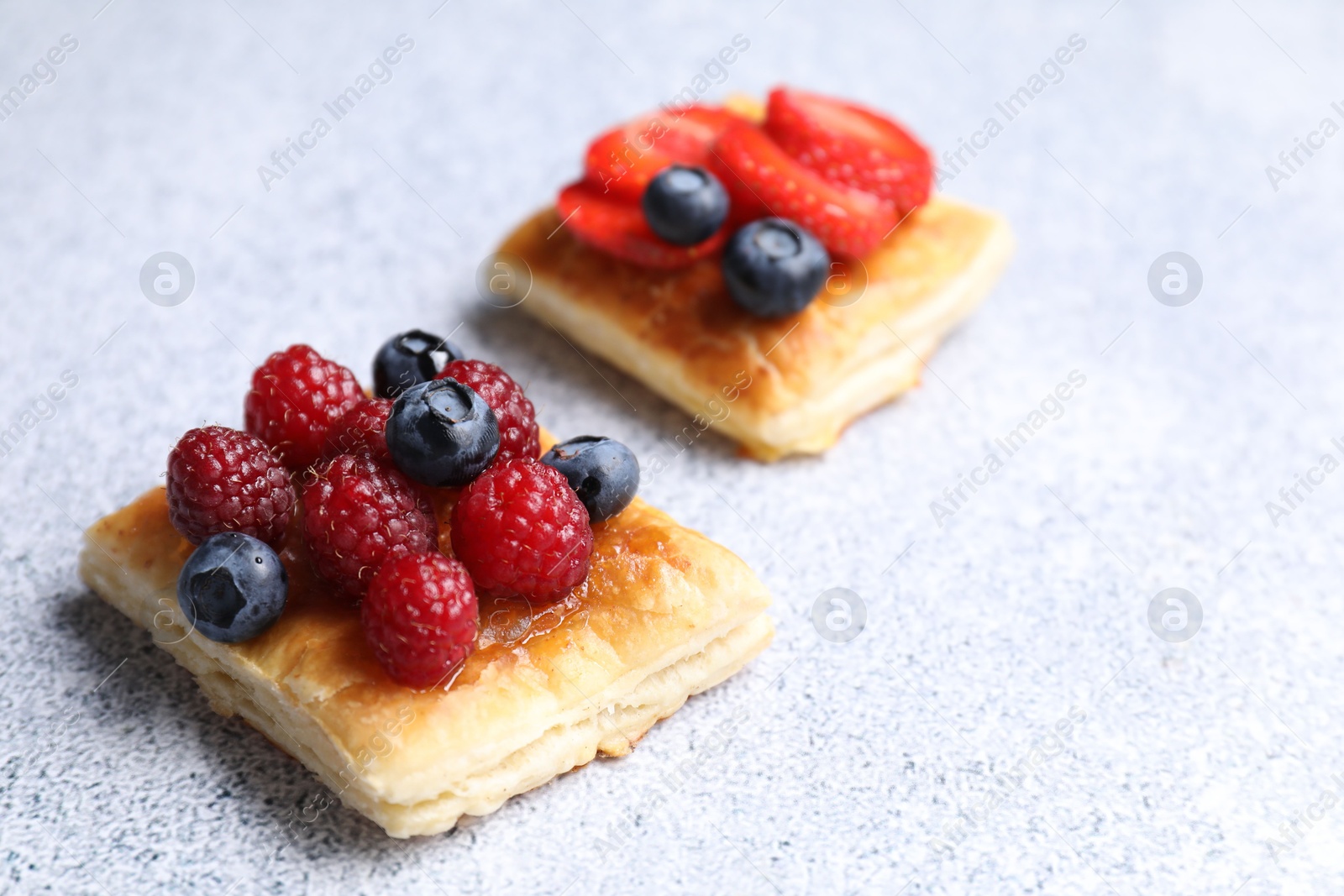 Photo of Tasty puff pastries with berries on light grey table, closeup. Space for text