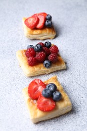 Tasty puff pastries with berries on light grey table