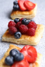 Photo of Tasty puff pastries with berries on light grey table, closeup