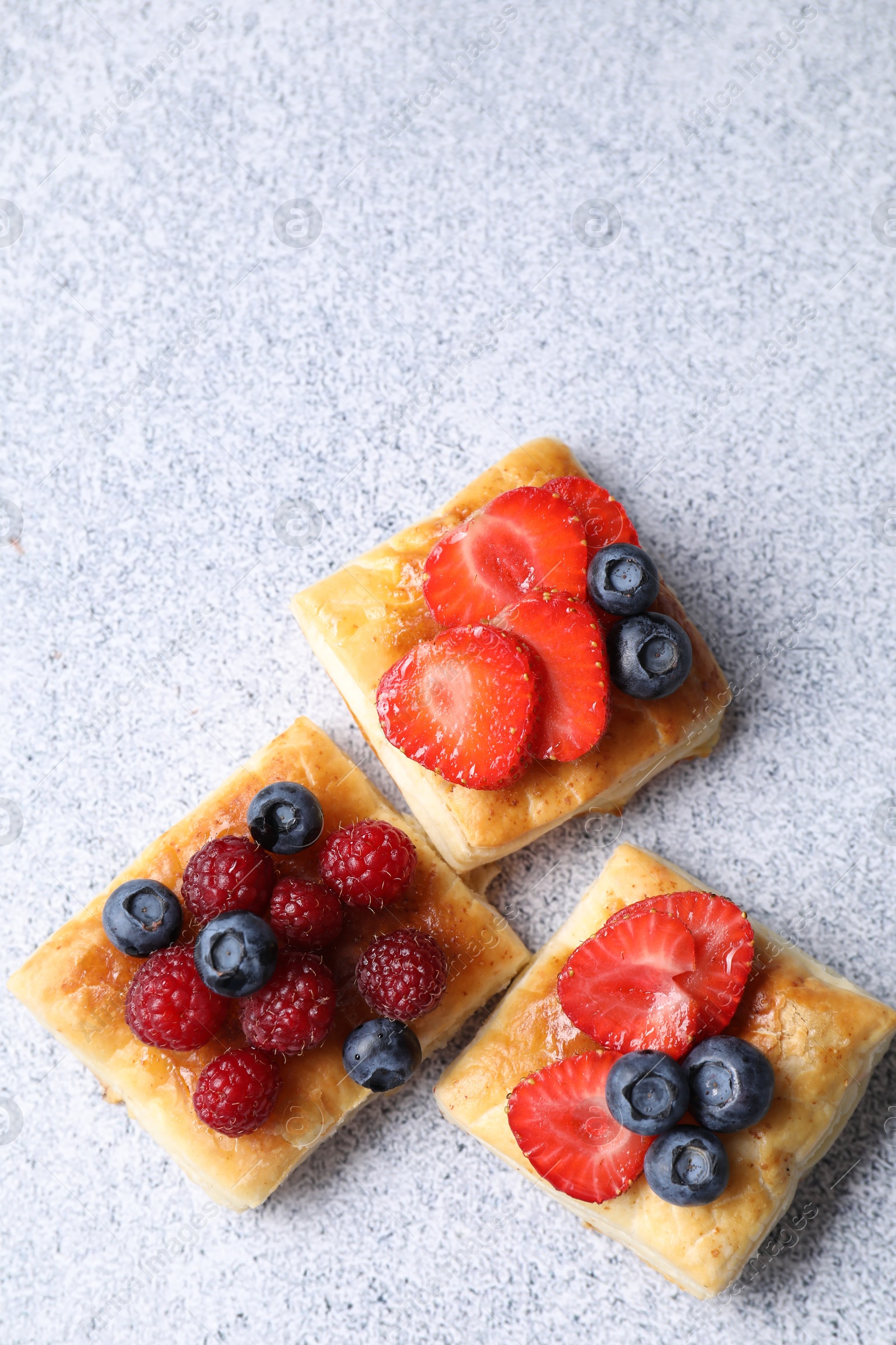 Photo of Tasty puff pastries with berries on light grey table, flat lay. Space for text