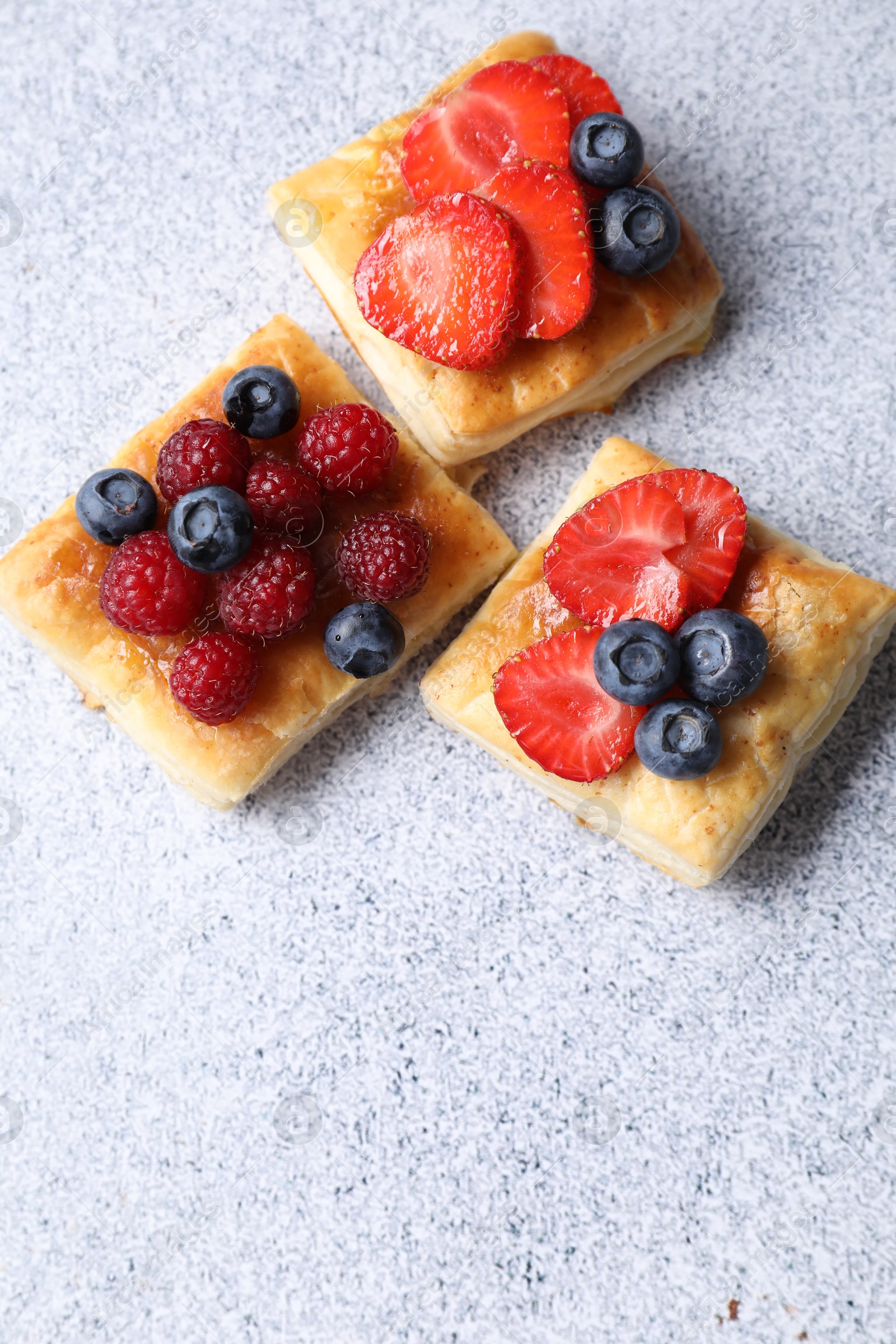 Photo of Tasty puff pastries with berries on light grey table, flat lay. Space for text