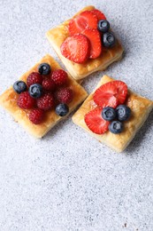 Photo of Tasty puff pastries with berries on light grey table, flat lay. Space for text