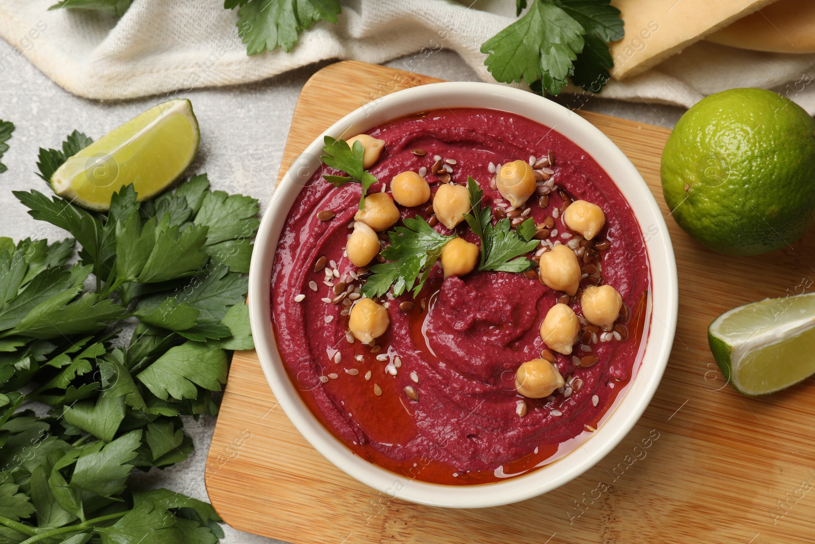 Photo of Tasty beet hummus with chickpeas in bowl, parsley and lime on light table, flat lay