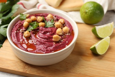 Photo of Tasty beet hummus with chickpeas and parsley in bowl on light table, closeup